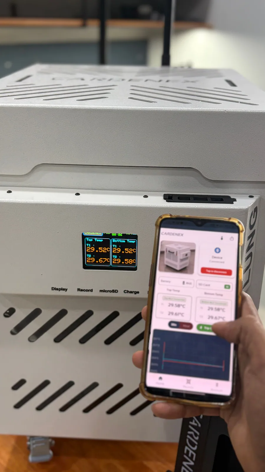 Mobile app showing live temperature readings held up next to the transport box display