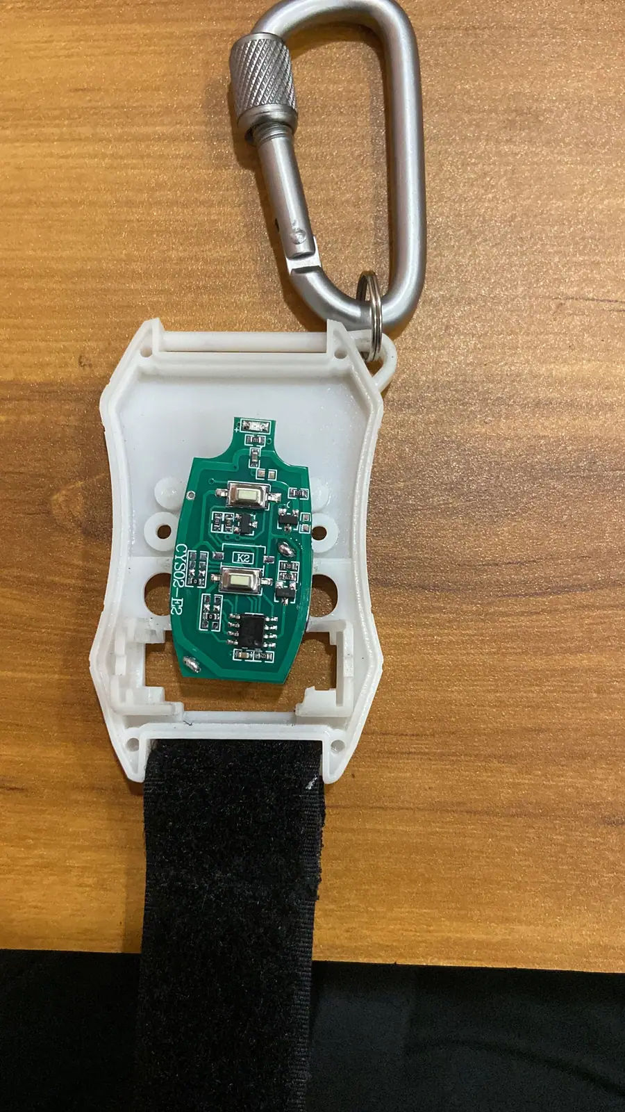 Wearable remote housing opened to show its custom PCB, with a carabiner and strap