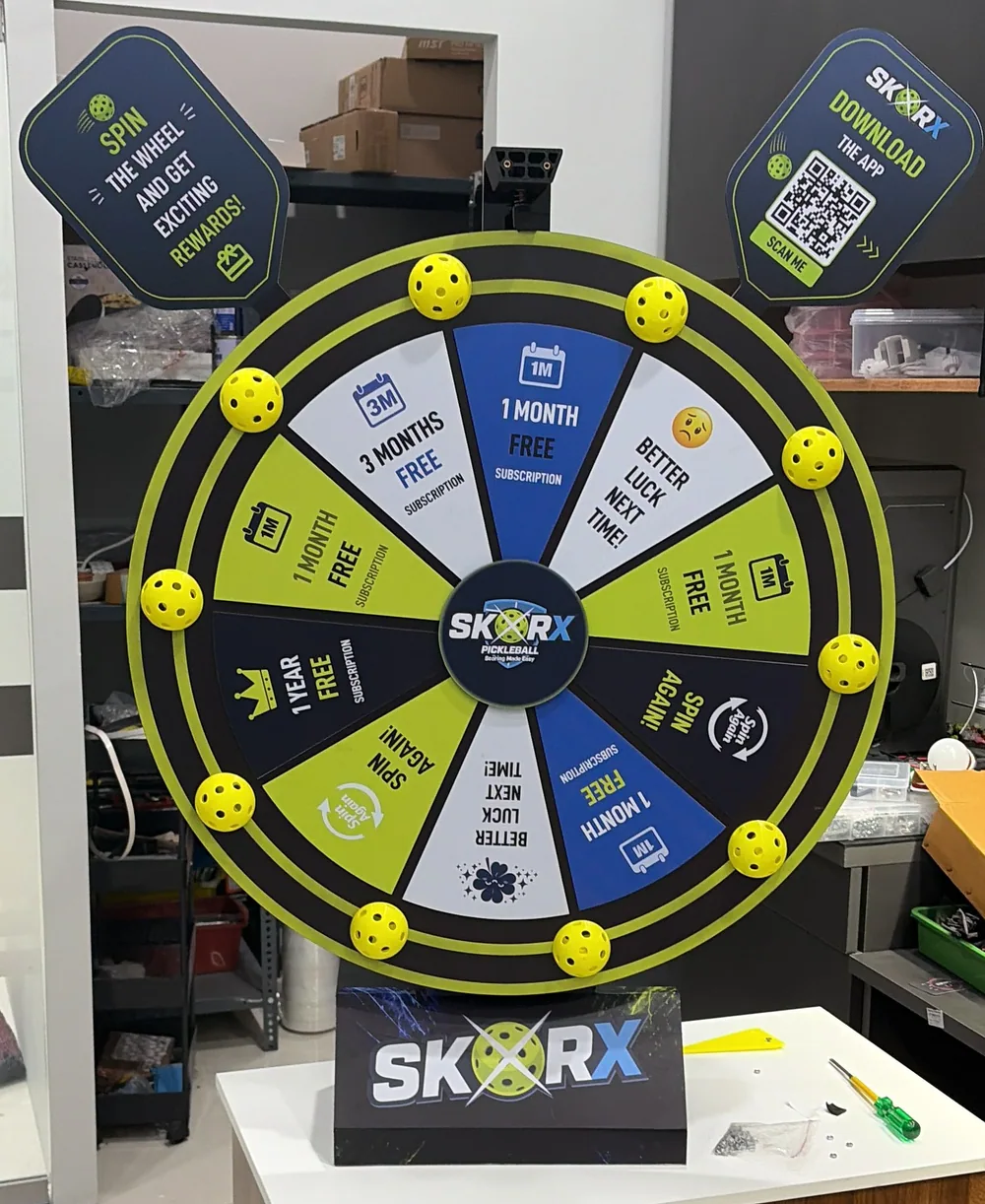 Finished SkorX spin wheel with prize segments, pickleball balls on the rim and download-the-app signs