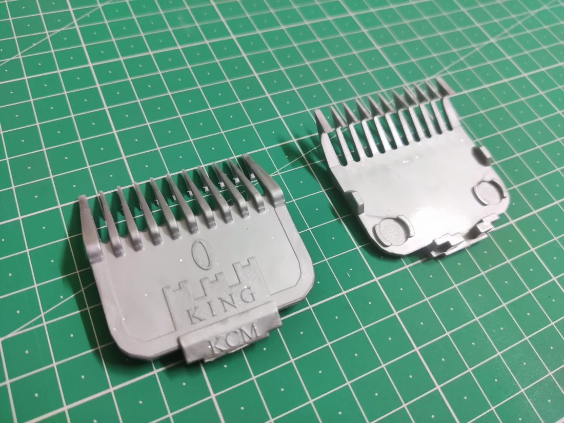 Two injection-molded trimmer guards, front and back, on a cutting mat