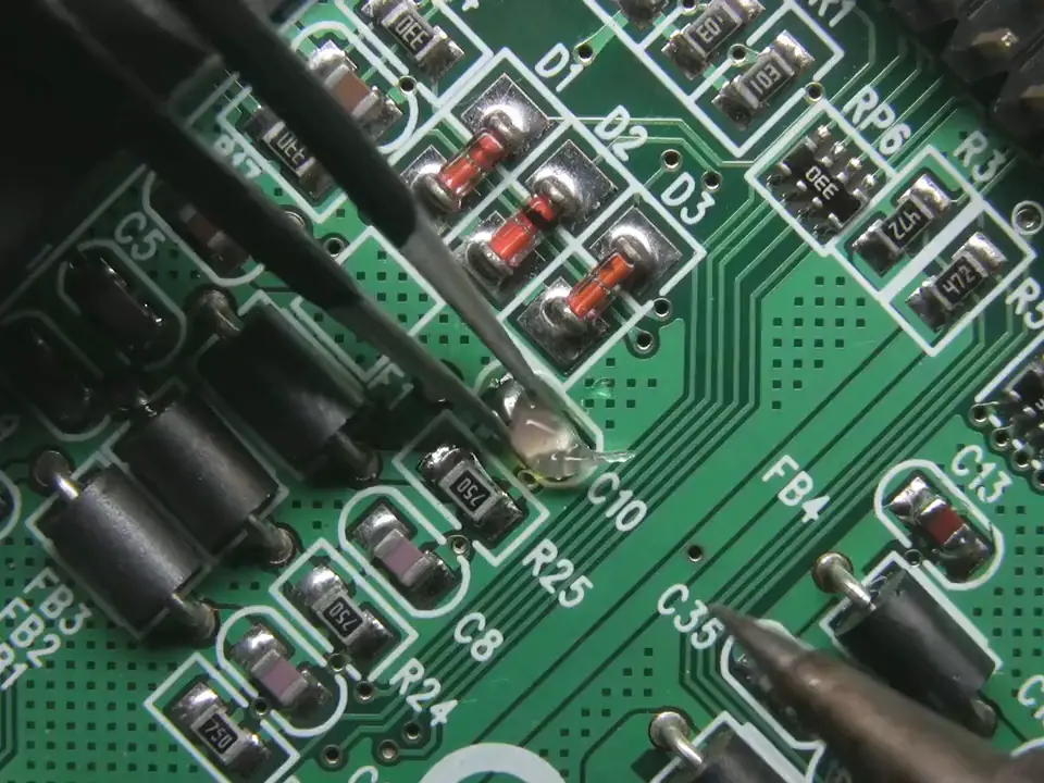 Close-up of a soldering iron joining a component on a green printed circuit board